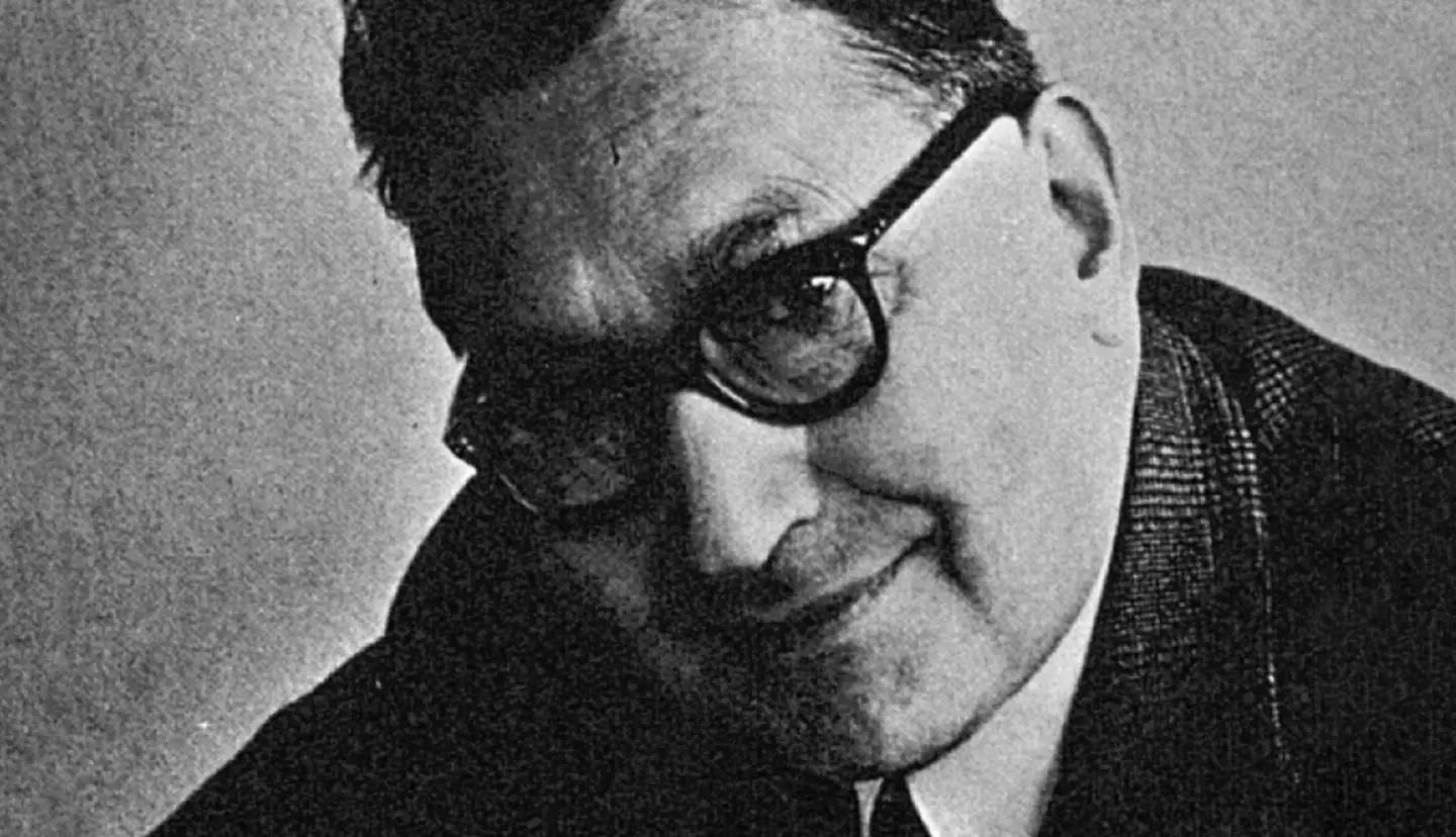 Portrait en noir et blanc de Raoul Perret pour Universal Genève Magazine, en lunettes rondes et veste sombre