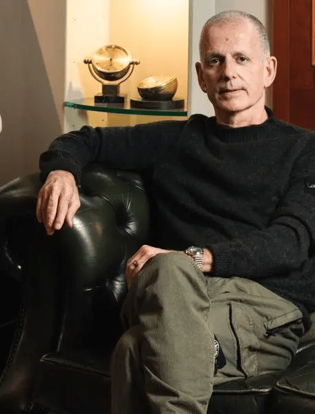 Luca Mignini assis dans un fauteuil en cuir près de garde-temps dorés dans un portrait Universal Genève