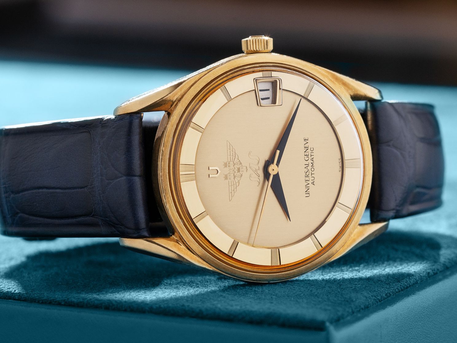 Montre automatique Universal Genève dorée avec cadran crème et bracelet en cuir bleu sur écrin doux